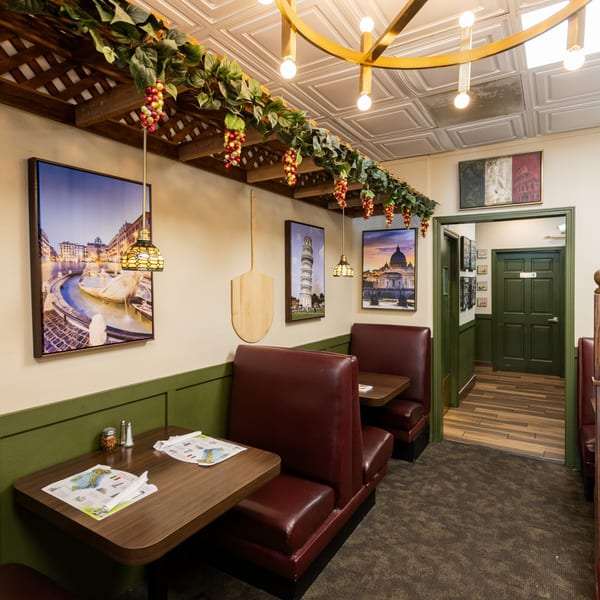 Cozy Italian restaurant interior with red booths, Italian landmark art, and decorative grapevines.