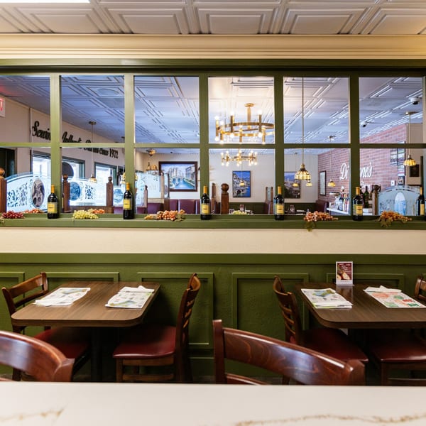 Interior of Di Leone's Italian Restaurant, with empty tables, chairs, and a decorative window looking into another dining area.