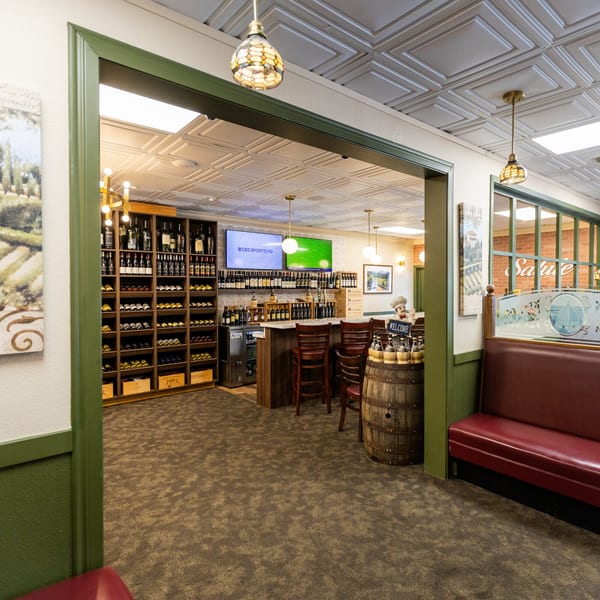 A wine bar area with shelves of wine bottles, a counter with stools, and two TVs.
