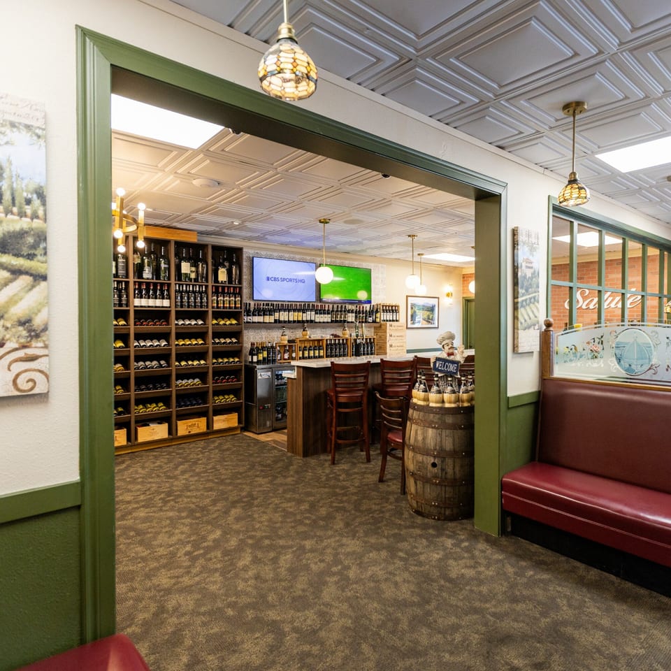 A wine bar area with shelves of wine bottles, a counter with stools, and two TVs.