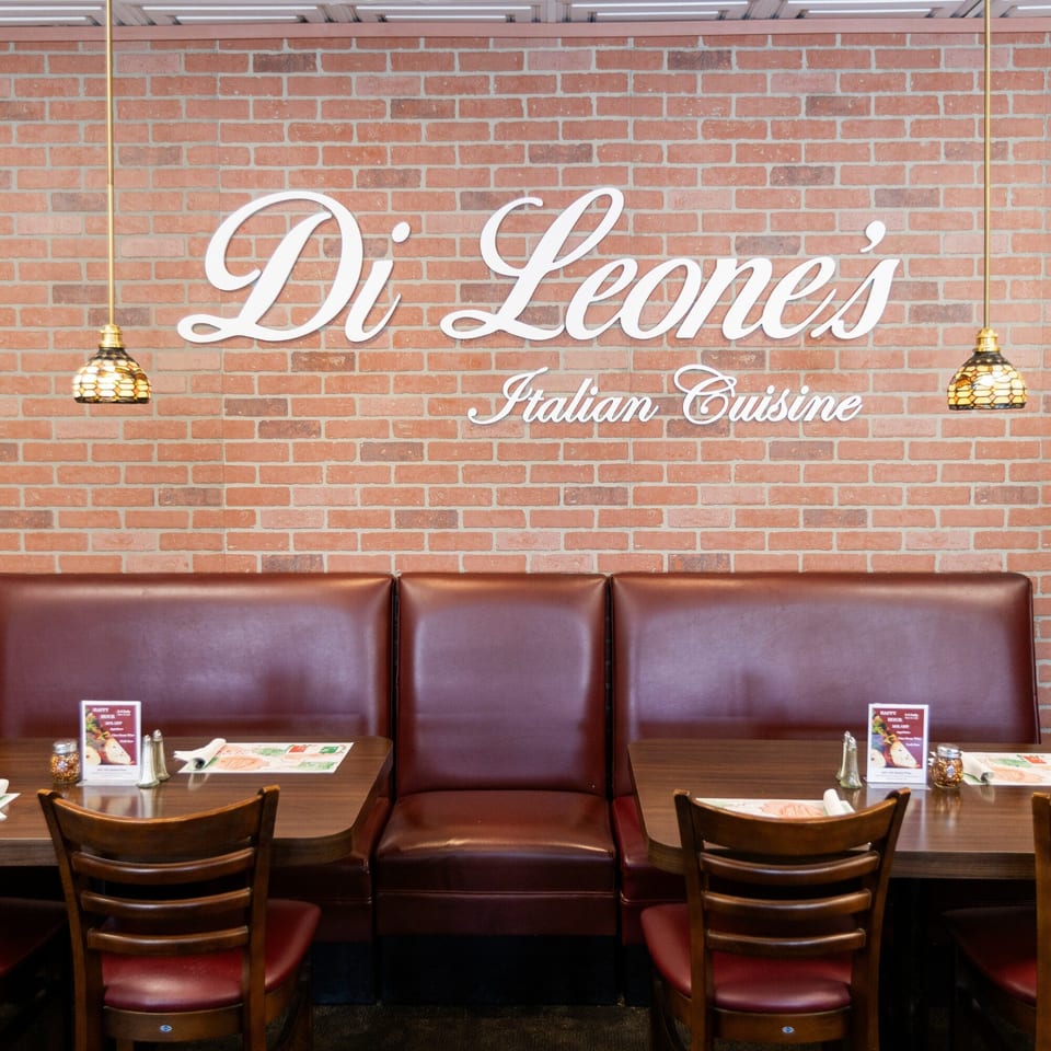 Di Leone's Italian Restaurant interior with a brick wall, brown booths, and wooden tables with chairs.