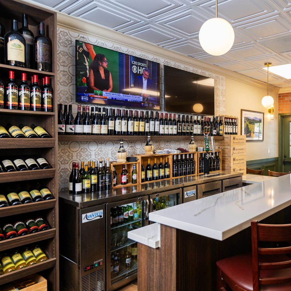 A well-stocked Italian restaurant bar with wine bottles, a TV, and a white countertop.