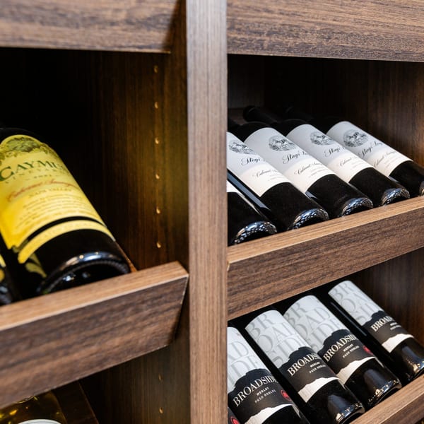 Wine bottles from various brands, including Caymus and Stags' Leap, stored in wooden racks.