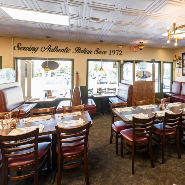 Interior of Di Leone's Italian Restaurant with empty tables, booths, and a sign reading "Serving Authentic Italian Since 1972".