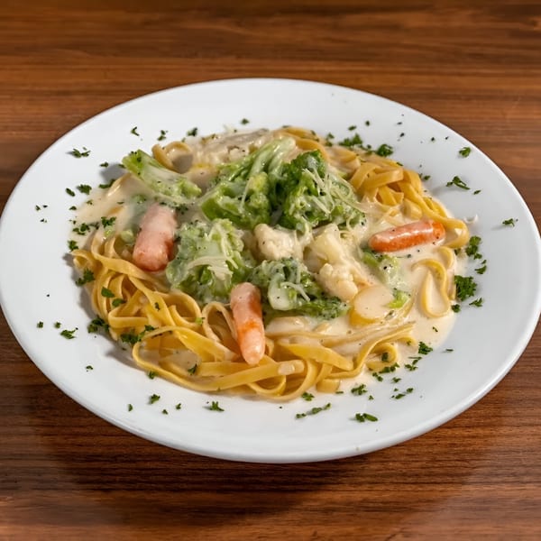 Fettuccine Alfredo with broccoli, carrots, and cauliflower in a creamy white sauce, garnished with parsley.