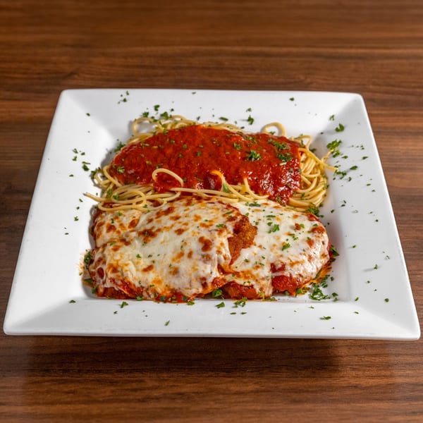 Chicken parmesan with melted cheese and spaghetti with red sauce, garnished with parsley on a white plate.