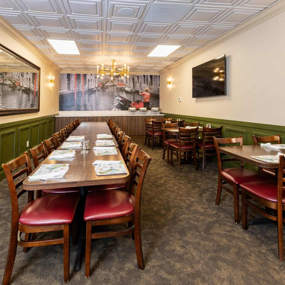 Di Leone's Italian Restaurant dining room with long tables, red chairs, and a Venice mural.