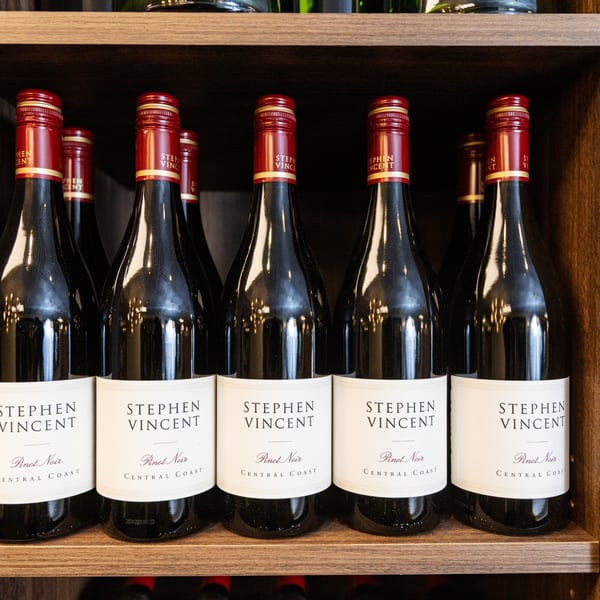 Rows of Stephen Vincent Pinot Noir wine bottles with red foil tops on wooden shelves.