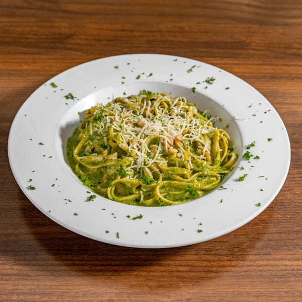 Di Leone's pesto pasta with pine nuts and parmesan cheese in a white bowl on a wooden table.