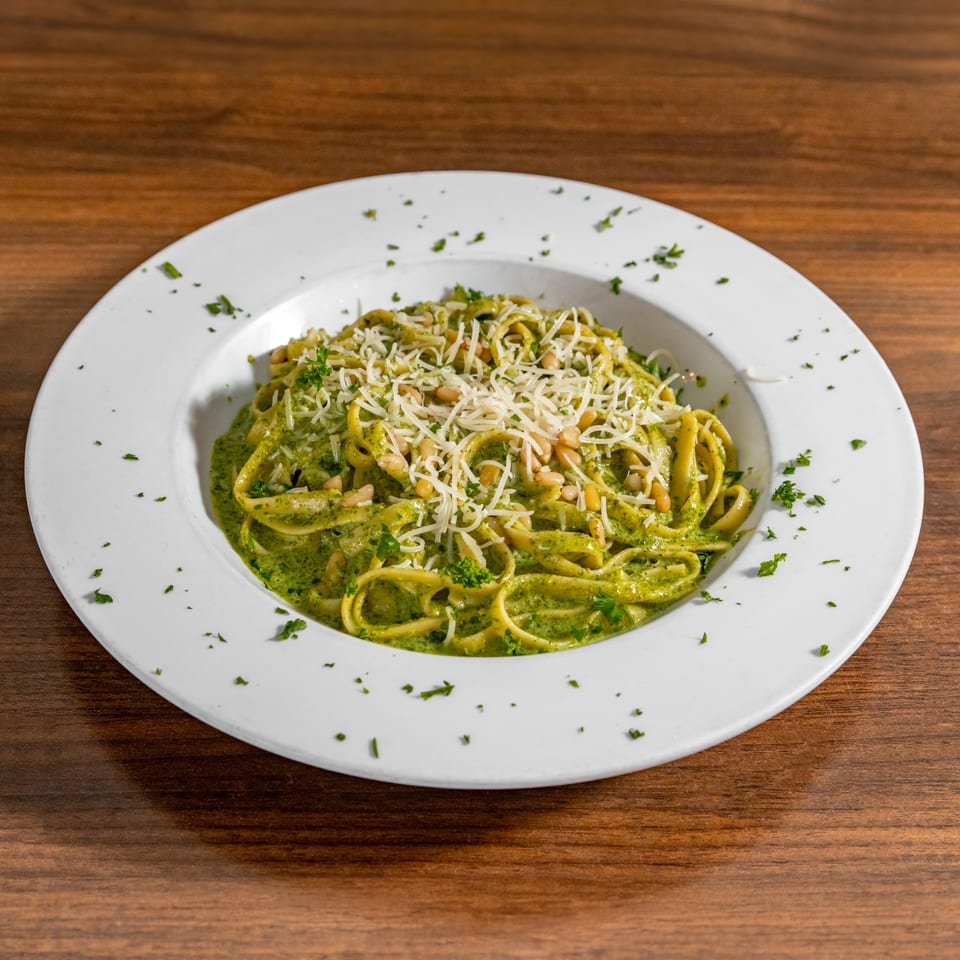 Di Leone's pesto pasta with pine nuts and parmesan cheese in a white bowl on a wooden table.