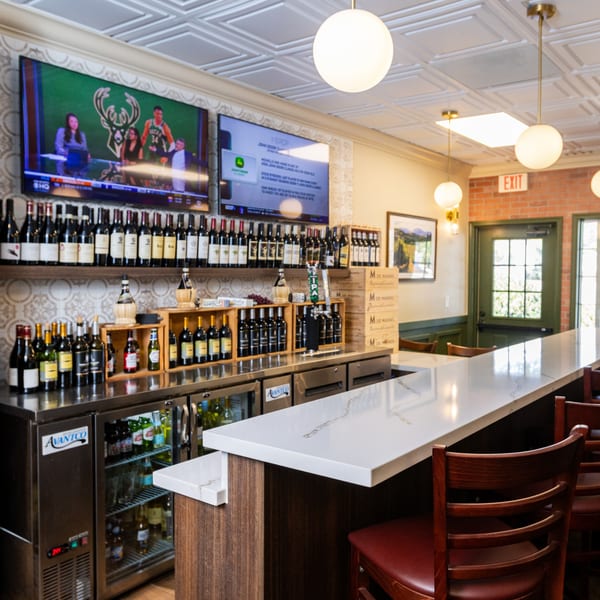 A well-stocked bar at Di Leone's Italian Restaurant with wine bottles, beer taps, and TVs showing sports.