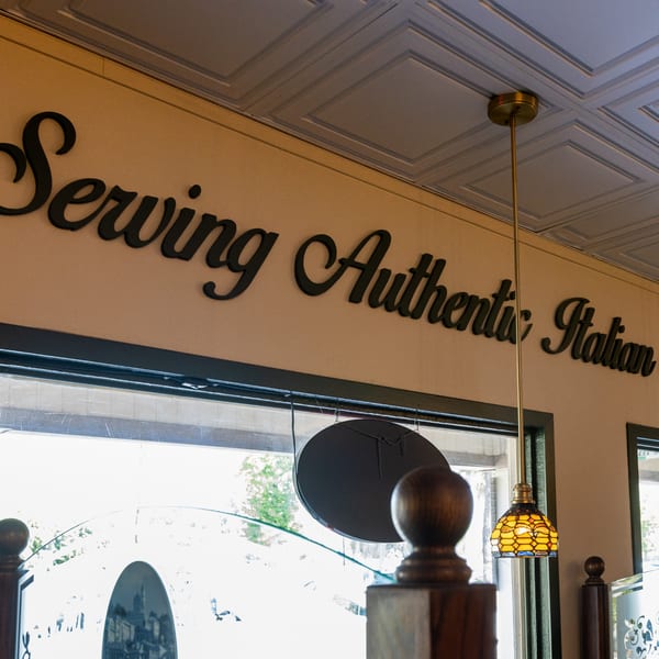 Di Leone's sign reads "Serving Authentic Italian" above a window with a hanging light fixture.