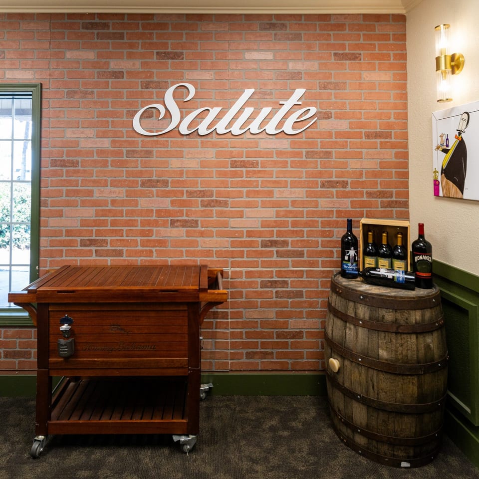 A brick wall with a "Salute" sign, a wooden cooler, and wine bottles on a barrel.