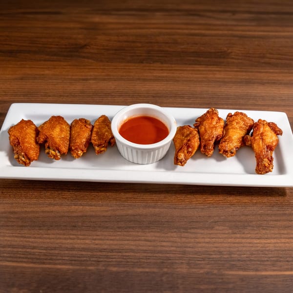 Golden-brown chicken wings with a side of red hot sauce on a white rectangular plate.