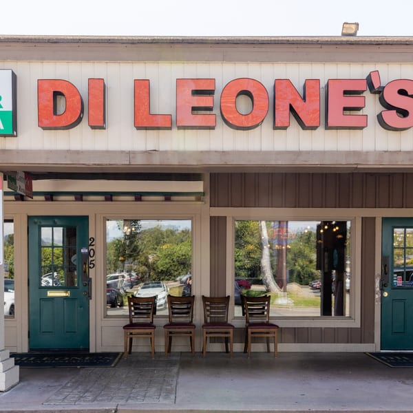 Di Leone's Italian Restaurant storefront with large red letters, green doors, and four chairs outside.