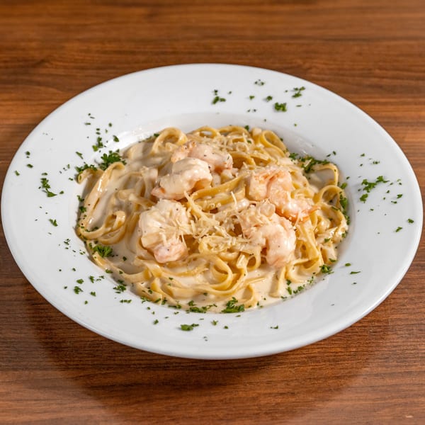 Creamy shrimp fettuccine Alfredo with grated cheese and parsley on a white plate.