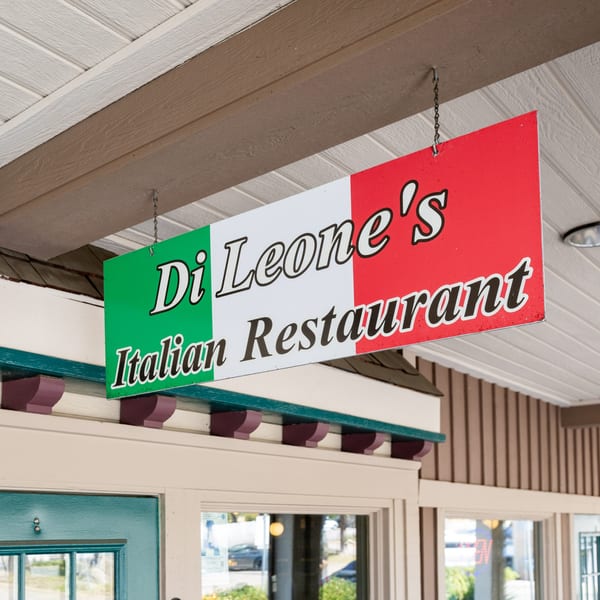 Di Leone's Italian Restaurant sign, designed like the Italian flag, hangs above a teal door.