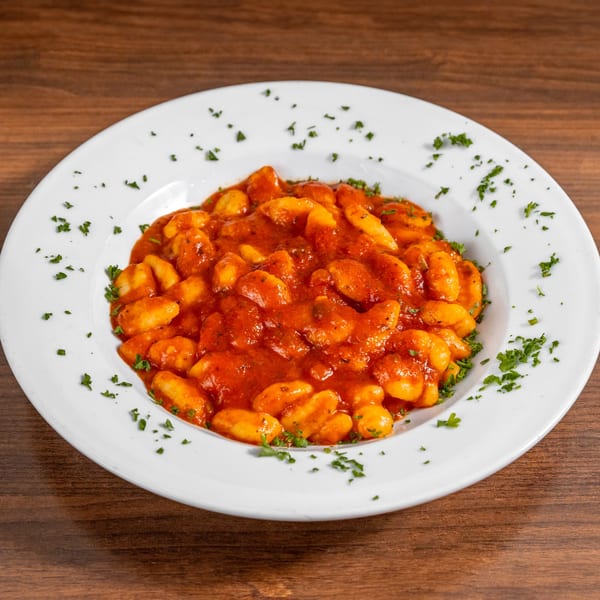 Di Leone's Italian Restaurant gnocchi in rich red tomato sauce, garnished with fresh parsley on a white plate.