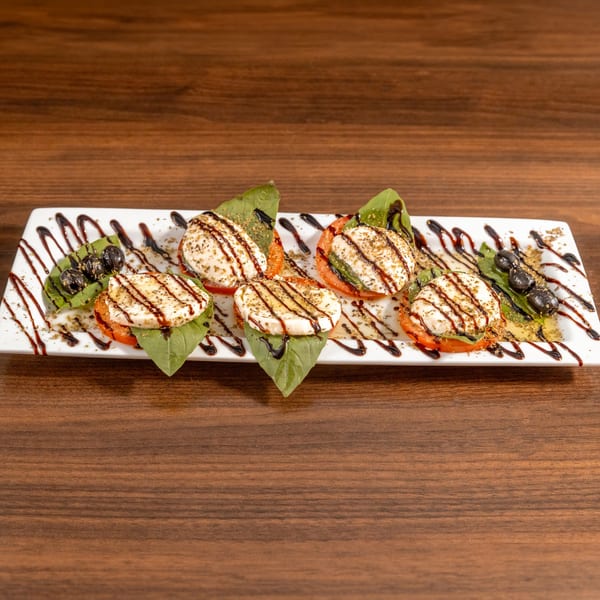 Caprese salad with mozzarella, tomatoes, basil, olives, and balsamic glaze on a white plate.
