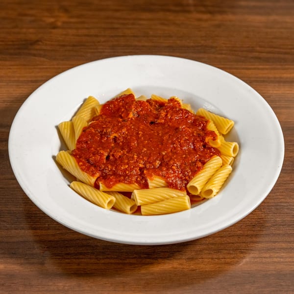 A white plate of rigatoni pasta covered in a rich, red meat sauce on a wooden table.