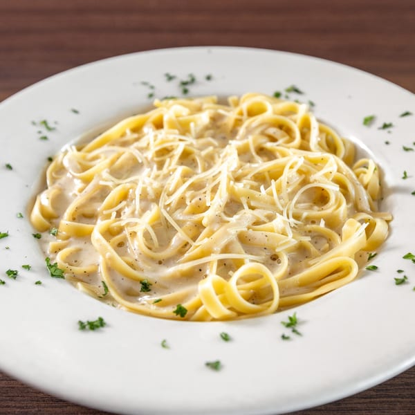 Creamy fettuccine alfredo with grated cheese and parsley on a white plate at Di Leone's Italian Restaurant.