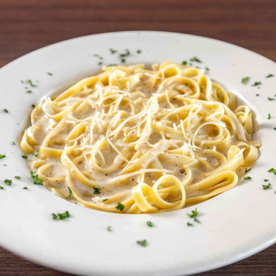 Creamy fettuccine alfredo with grated cheese and parsley on a white plate at Di Leone's Italian Restaurant.